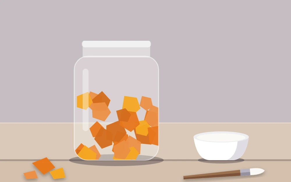 A glass jar half covered in overlapping torn orange tissue, with a brush and a dish of glue