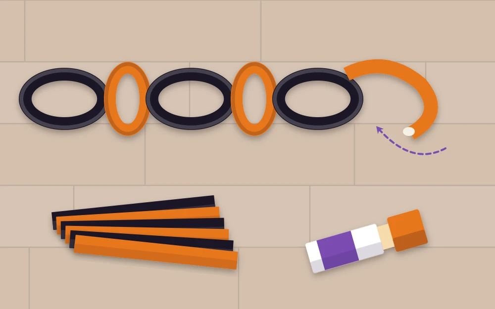 Black and orange paper chain links being joined beside stacked strips and a glue stick